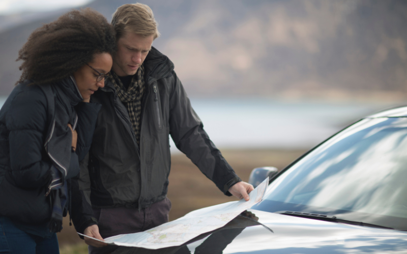 Young couple consulting road map outside their vehicle